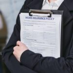Gros plan d'une personne détenant une police d'assurance habitation sur un presse-papiers, capturé à l'intérieur.